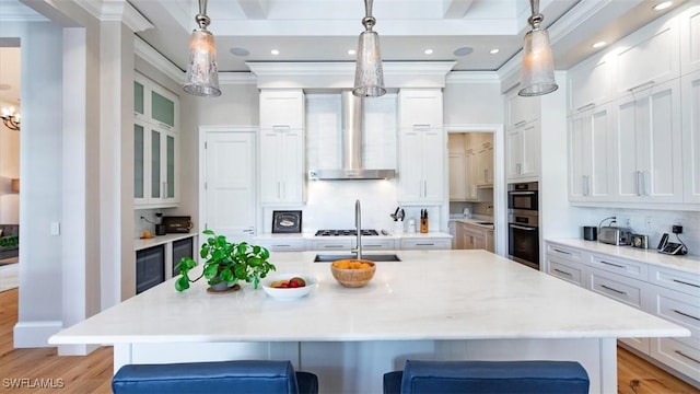 kitchen featuring light wood-type flooring, white cabinets, wall chimney range hood, and a breakfast bar area