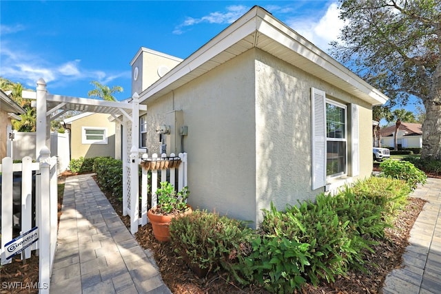 view of side of home featuring fence, a pergola, and stucco siding