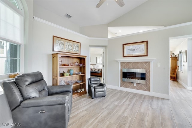 living area featuring visible vents, baseboards, lofted ceiling, a tile fireplace, and light wood-style floors