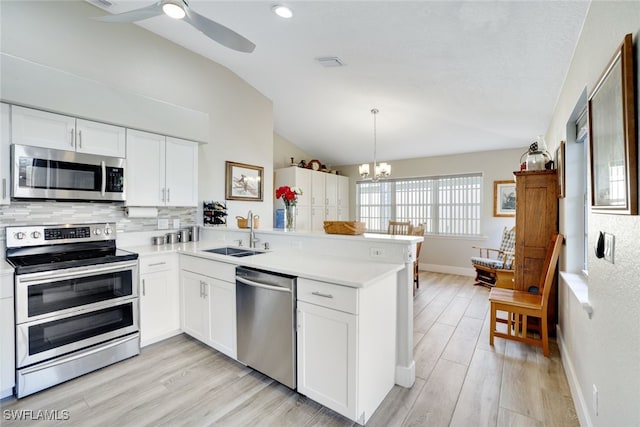 kitchen featuring a sink, tasteful backsplash, appliances with stainless steel finishes, a peninsula, and lofted ceiling