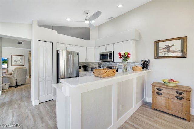 kitchen featuring backsplash, white cabinetry, stainless steel appliances, a peninsula, and light countertops