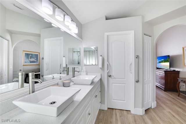 bathroom featuring a sink, wood finished floors, double vanity, and vaulted ceiling