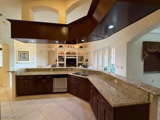 kitchen with light stone countertops, sink, stainless steel dishwasher, a towering ceiling, and light tile patterned flooring