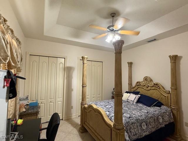 bedroom with ceiling fan, a raised ceiling, and multiple closets