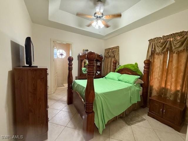 bedroom with light tile patterned flooring, a tray ceiling, ceiling fan, and ensuite bathroom