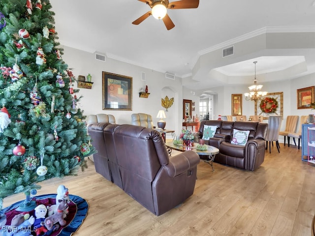 living room featuring ceiling fan with notable chandelier, light wood-type flooring, a raised ceiling, and ornamental molding