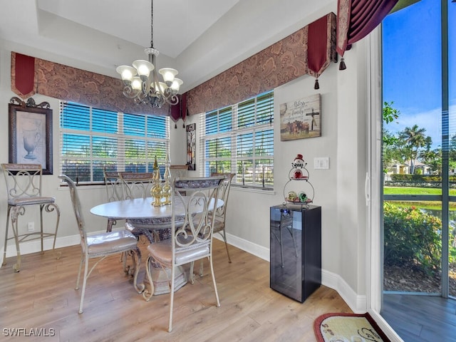 dining room featuring a notable chandelier, a raised ceiling, light wood-type flooring, and beverage cooler