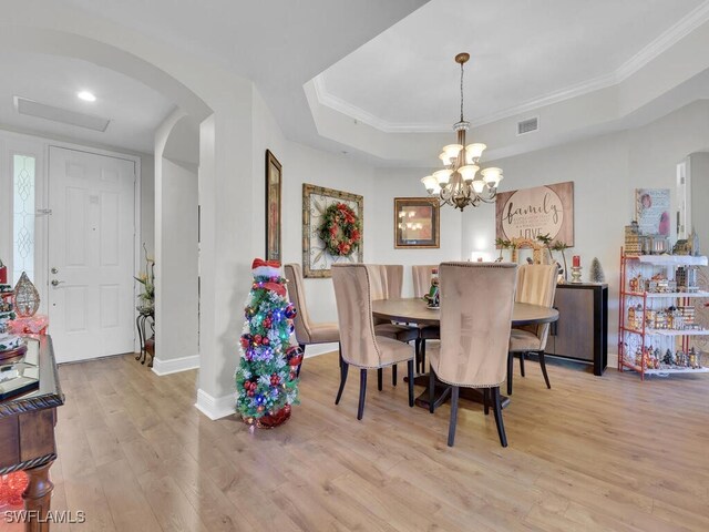 dining space with a chandelier, light wood-type flooring, ornamental molding, and a tray ceiling