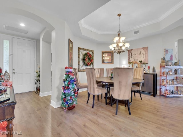 dining area featuring light wood-style flooring, a tray ceiling, arched walkways, and crown molding