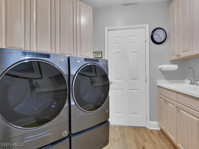 clothes washing area featuring light wood-type flooring, cabinet space, washing machine and dryer, and a sink