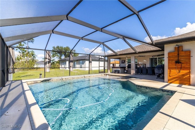 view of pool featuring a yard, a patio, glass enclosure, and ceiling fan