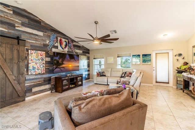 living room featuring a barn door, wooden walls, light tile patterned floors, and lofted ceiling