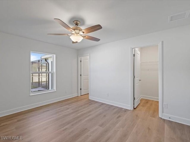 unfurnished bedroom featuring a walk in closet, ceiling fan, a closet, and light wood-type flooring