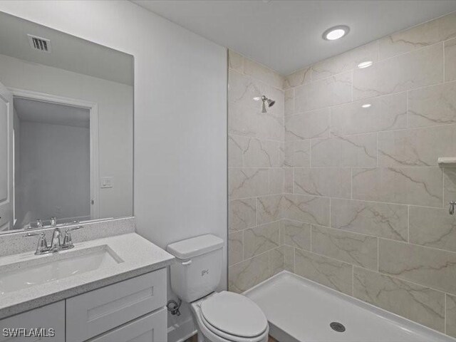 bathroom featuring a tile shower, vanity, and toilet