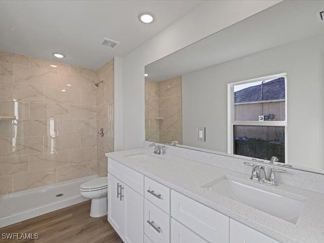 bathroom featuring toilet, vanity, wood-type flooring, and tiled shower