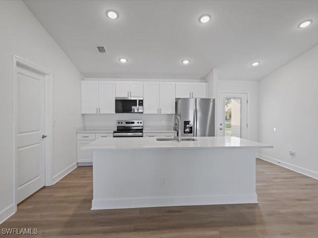 kitchen with hardwood / wood-style floors, sink, an island with sink, appliances with stainless steel finishes, and white cabinetry