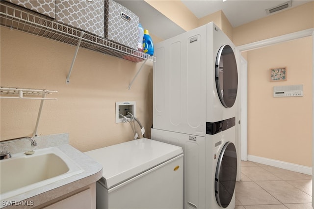 laundry area with light tile patterned floors, stacked washer and dryer, and sink