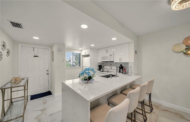 kitchen featuring kitchen peninsula, decorative backsplash, white appliances, white cabinets, and a breakfast bar area