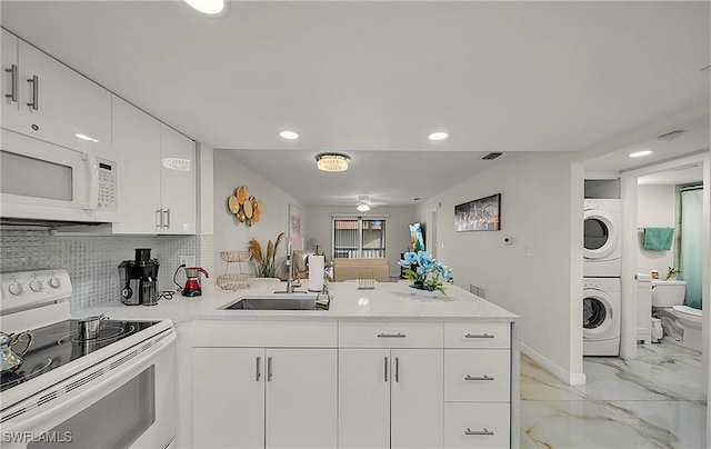 kitchen with white cabinetry, sink, stacked washing maching and dryer, kitchen peninsula, and white appliances