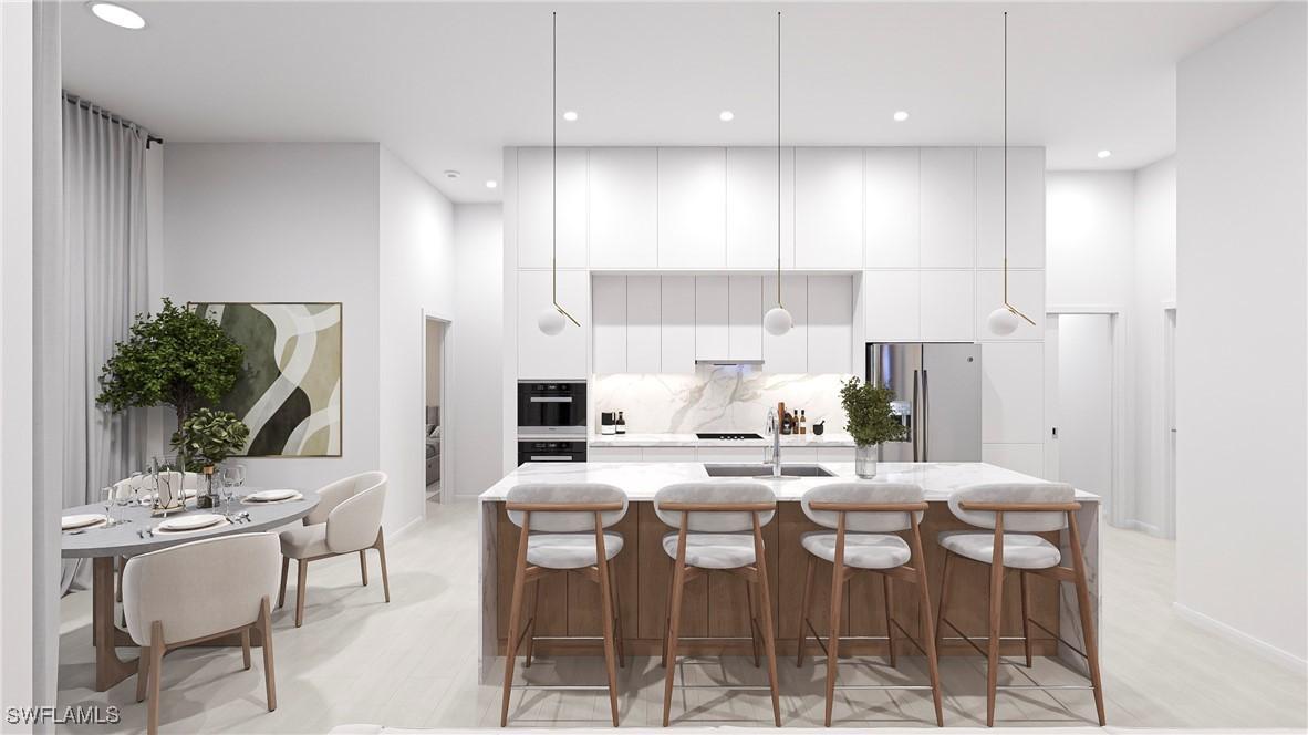 kitchen featuring white cabinets, stainless steel fridge, an island with sink, and tasteful backsplash