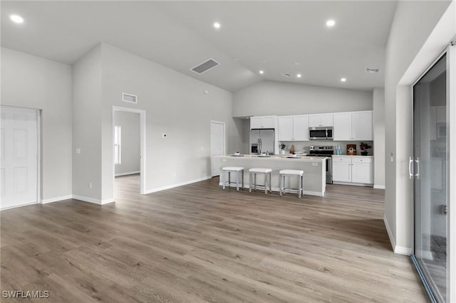 kitchen featuring white cabinetry, stainless steel appliances, high vaulted ceiling, an island with sink, and a breakfast bar