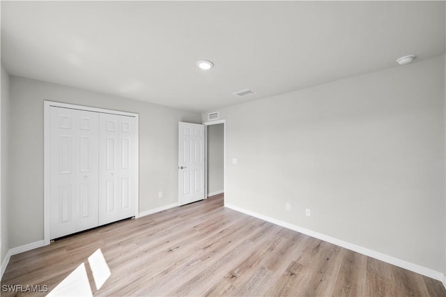 unfurnished bedroom featuring visible vents, a closet, baseboards, and wood finished floors