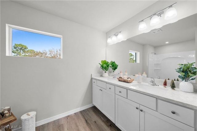 bathroom featuring double vanity, wood finished floors, a sink, and baseboards