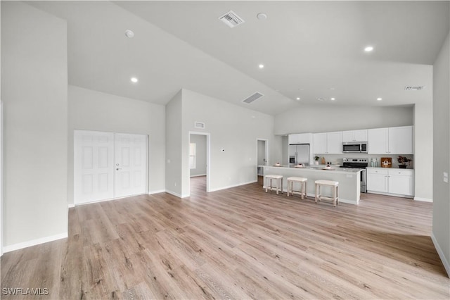 unfurnished living room with high vaulted ceiling, light wood finished floors, visible vents, and baseboards