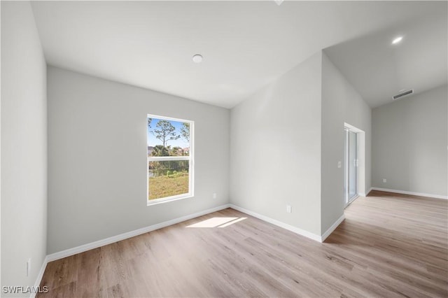 empty room with vaulted ceiling, light wood finished floors, and baseboards