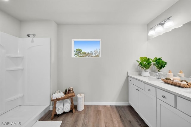 bathroom with wood finished floors, walk in shower, vanity, and baseboards