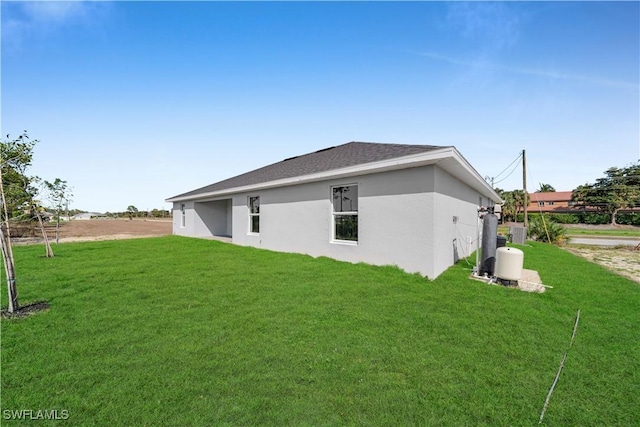 back of property with roof with shingles, a lawn, and stucco siding