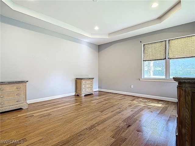 spare room with a tray ceiling and wood-type flooring