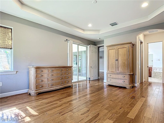 unfurnished bedroom featuring ensuite bath, wood-type flooring, and a tray ceiling