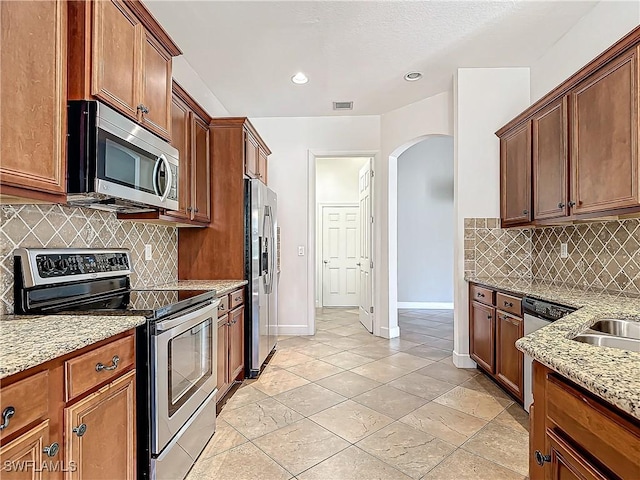 kitchen featuring light stone countertops, appliances with stainless steel finishes, decorative backsplash, and light tile patterned floors