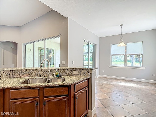 kitchen with decorative light fixtures, light tile patterned flooring, light stone countertops, and sink