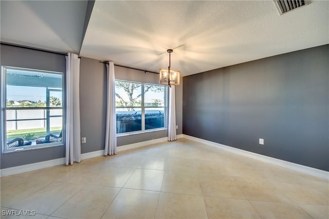 spare room featuring light tile patterned flooring, a healthy amount of sunlight, a textured ceiling, and an inviting chandelier