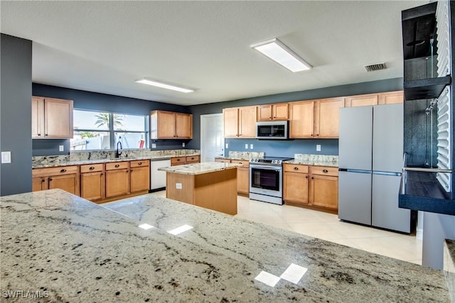 kitchen with a center island, sink, light stone countertops, appliances with stainless steel finishes, and light tile patterned flooring