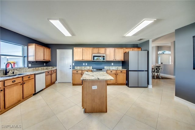 kitchen featuring light stone countertops, appliances with stainless steel finishes, sink, light tile patterned floors, and a kitchen island