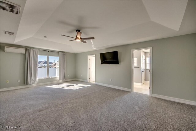 unfurnished room with a tray ceiling, a wall mounted AC, ceiling fan, and light carpet