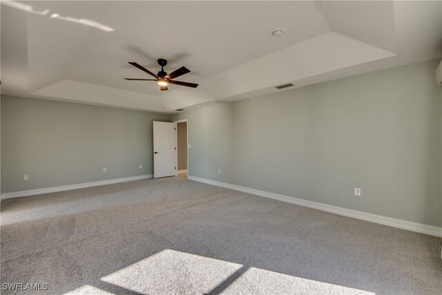 spare room featuring ceiling fan, light colored carpet, and a tray ceiling