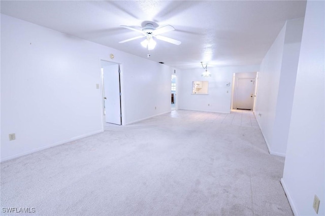 spare room featuring ceiling fan with notable chandelier and light carpet