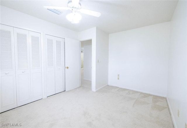 unfurnished bedroom with ceiling fan, light colored carpet, and two closets