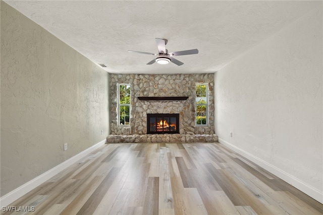 unfurnished living room featuring a stone fireplace, light hardwood / wood-style flooring, and a healthy amount of sunlight