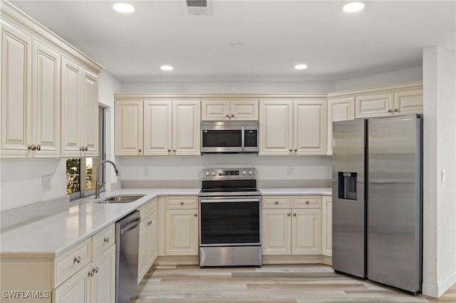 kitchen with sink, cream cabinetry, stainless steel appliances, and light wood-type flooring