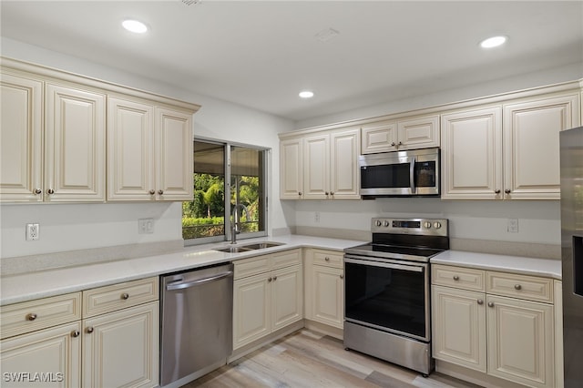 kitchen with cream cabinets, sink, stainless steel appliances, and light hardwood / wood-style flooring