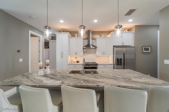 kitchen with visible vents, a sink, stainless steel appliances, wall chimney range hood, and a large island with sink