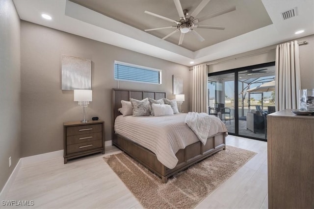 bedroom featuring light wood-style floors, a raised ceiling, baseboards, and access to outside