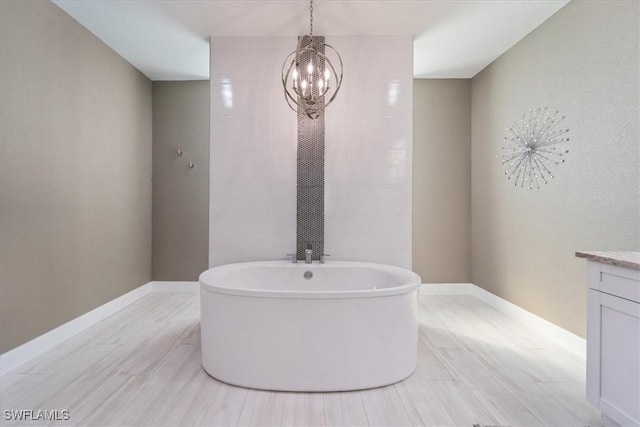 full bath featuring a freestanding tub, baseboards, a notable chandelier, and vanity