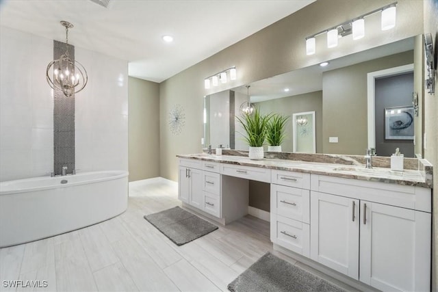 full bathroom with double vanity, a freestanding tub, a notable chandelier, and a sink