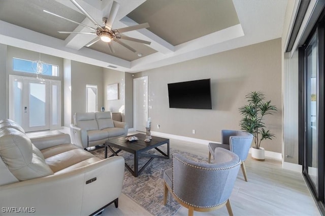 living room with visible vents, light wood-style flooring, a tray ceiling, baseboards, and ceiling fan